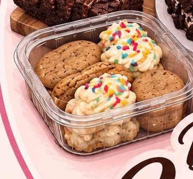 A box of freshly baked cookies topped with buttercream and sprinkles